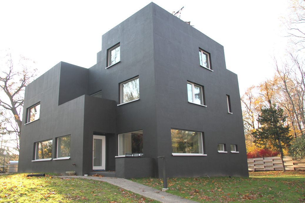 Cubic modernist house finished in dark grey, with white-framed windows, in autumn