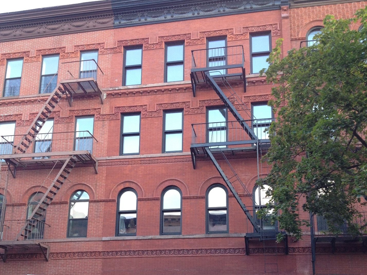 Four-story red brick apartment building with ornate terracotta bands and new dark windows