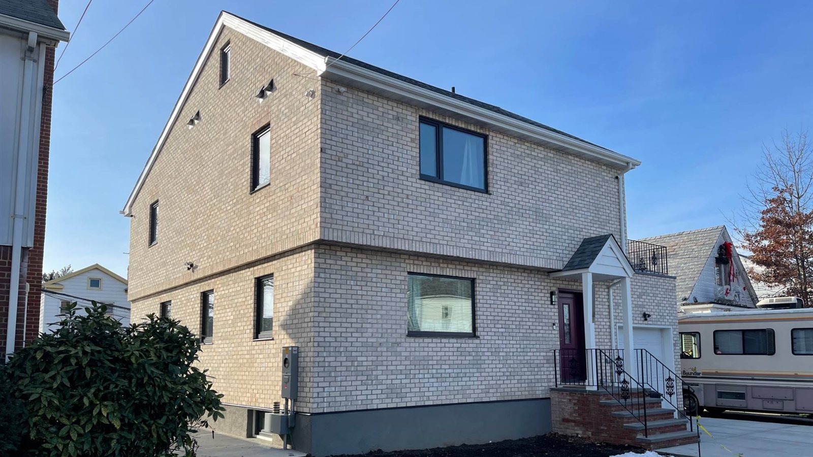 Single-family house with new pale thin brick cladding, dark windows, and a small entry porch